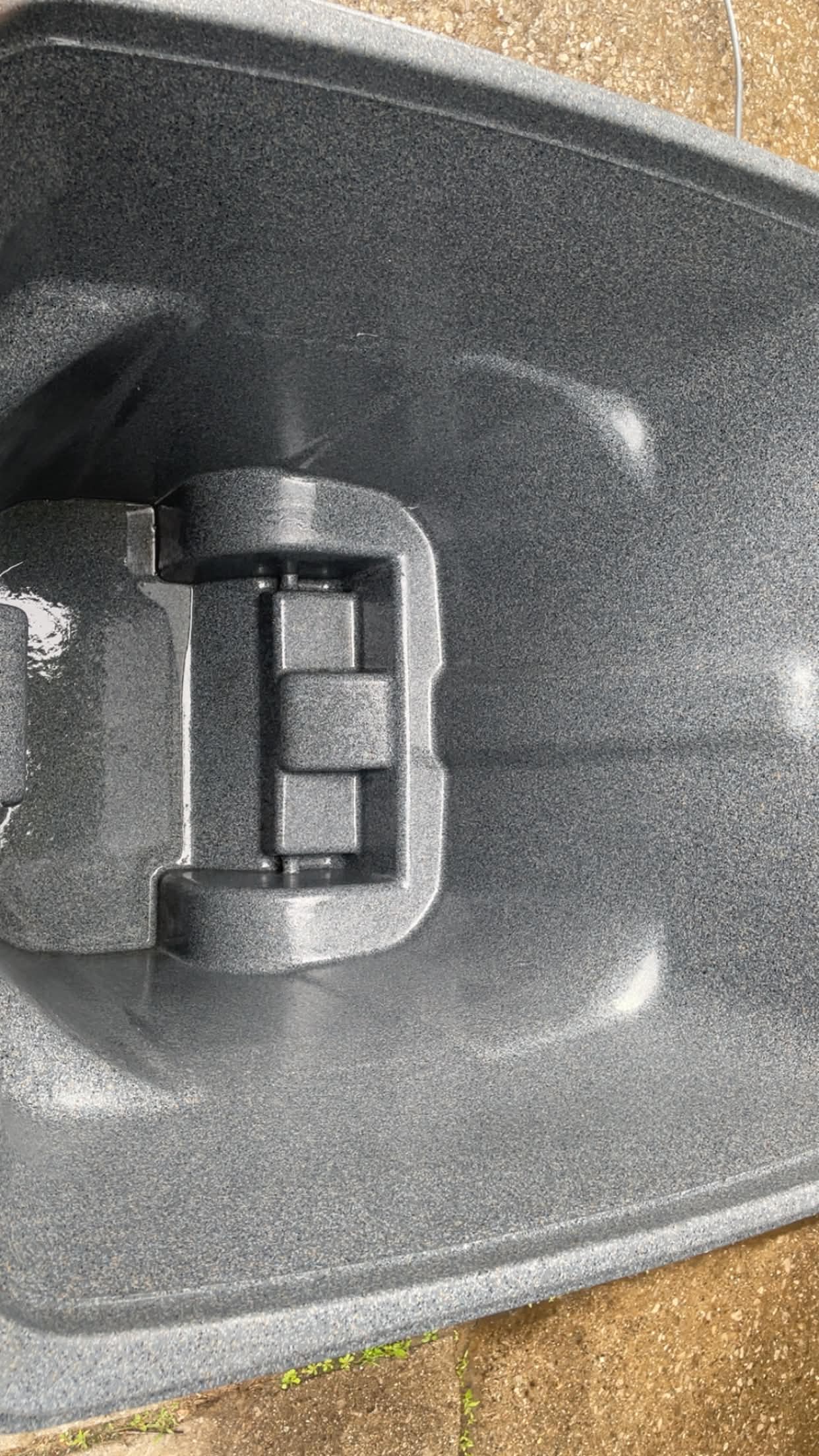 Inside a gray speckled plastic bin showing the molded hinge and a wet interior surface.