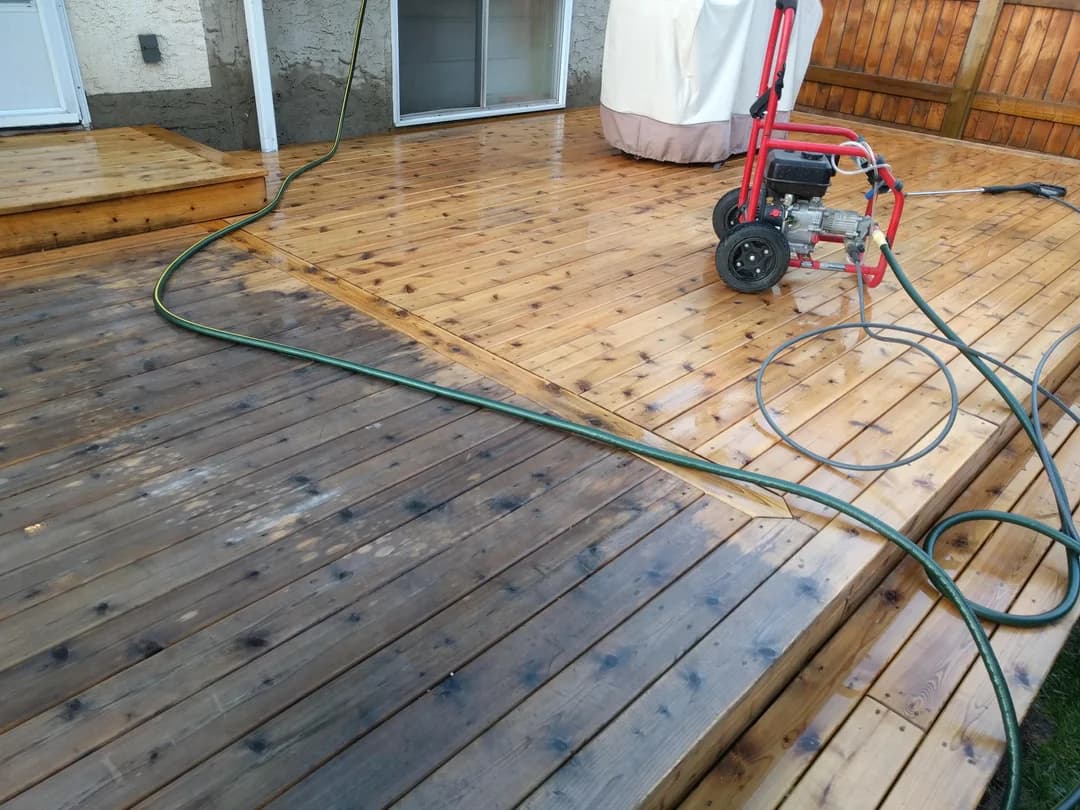 Dramatic contrast between dirty and freshly power-washed wood on a deck with a red pressure washer.